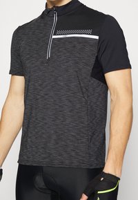 Mand iført en sort og mørkegrå kortærmet cykeltrøje med lynlås foran og sorte polstrede cykelshorts.