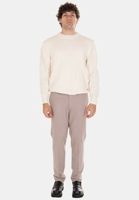 Maglione lavorato a maglia crema, pantaloni beige a taglio affusolato e scarpe di pelle nere. Il maglione ha una scollatura rotonda e una finitura strutturata, mentre i pantaloni sono lisci.