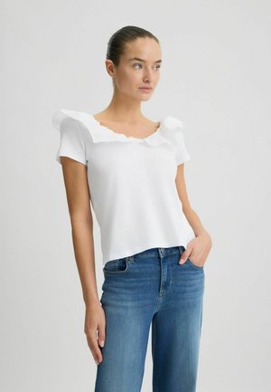 Top bianco a maniche corte con scollatura quadrata arricciata, abbinato a jeans in denim blu, caratterizzati da una vestibilità comoda e una texture in cotone morbido.