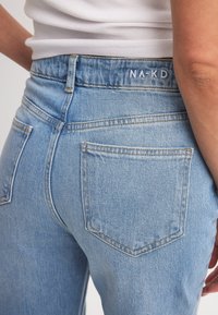 Vaaleansiniset farkut, joissa on korkea vyötärö, kaksi takataskua, hienovaraiset ompeleet ja brändäys vyötärönauhassa.