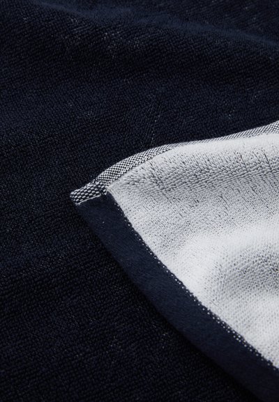 Navy textile featuring a textured surface; edged with a contrasting white trim that has a subtle checkered pattern.