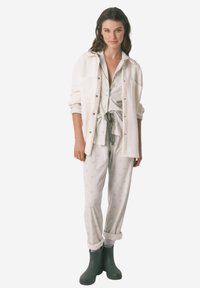 Completo da loungewear composto da una maglietta grigia chiara a motivi con vita allacciata e pantaloni abbinati, abbinato a una camicia bianca con bottoni e stivali verdi.
