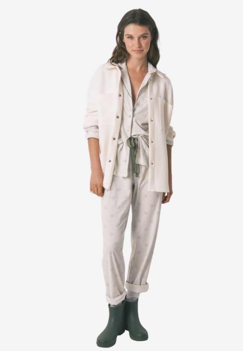 Completo da loungewear composto da una maglietta grigia chiara a motivi con vita allacciata e pantaloni abbinati, abbinato a una camicia bianca con bottoni e stivali verdi.