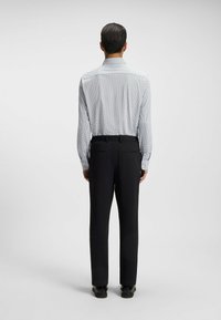 White shirt with small blue dots, buttoned collar, and long sleeves; paired with black textured trousers and black shoes.