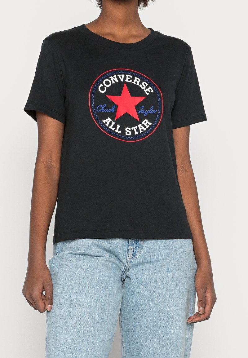 Camiseta de algodón negra con un gráfico redondo que presenta una estrella roja y el texto "Converse All Star" en azul en la parte delantera. Mangas cortas, corte relajado.