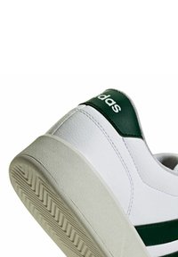 Zapatilla blanca con detalles verdes. Parte superior de cuero sintético, puntera redondeada y suela de goma texturizada con dibujo patrón. Marca en el talón.