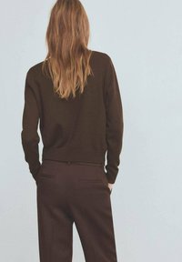 Brauner Strickpullover mit lockerem Schnitt, kombiniert mit dunkelbraunen Hosen mit subtiler Textur und Seitentaschen. Rückansicht gezeigt.