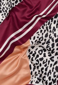 Μεταξένιο ύφασμα με σχέδιο λεοπάρδαλης, μπορντό ρίγες και τμήματα ροδάκινου, εμφανίζοντας ομαλές πτυχές και αντιθετικά μοτίβα.