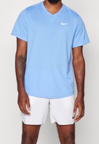 Blå Nike V-ringad t-shirt gjord av lätt tyg med korta ärmar, som har en liten vit logotyp på det övre vänstra bröstet.