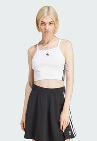 Biały krótki top na ramiączkach z cienkimi paskami i logo Adidas; zestawiony z czarną spódnicą z białymi paskami i elastycznym pasem.