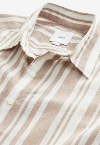 Beige en witte gestreepte linnen shirt met een button-down kraag en een label met de merknaam "NEXT." Gestructureerde, lichte stof.