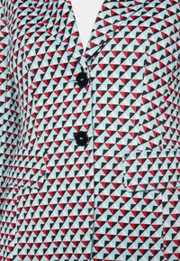 Blazer avec un motif géométrique en bleu, rouge et noir. Comprend deux grands boutons noirs, des revers en pointe et deux poches latérales.
