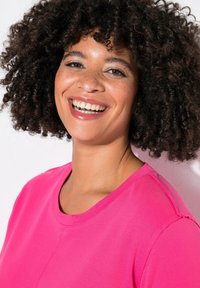 T-shirt rosa brillante con collo rotondo, maniche corte e dettagli delle cuciture visibili. Il tessuto appare morbido e liscio.