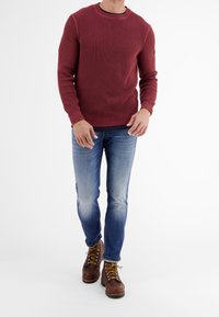 Bordeauxfärgad stickad tröja med ribbade ärmslut och nederkant, tillsammans med ljusblå blekta jeans och bruna snörstövlar med gula snören och strukturerad sula.