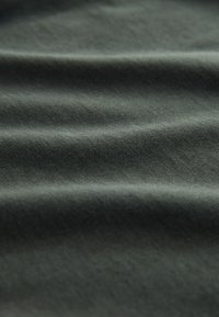 Tume roheline kangas pehme tekstuuriga, millel on peened kortsud ja sile pind. Materjal näib kerge ja vastupidav.