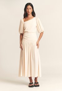 Krēmkrāsas midi kleita ar pūderveida piedurknēm un asimetrisku izgriezumu. Plūstoša silueta ar savilktu vidukli un mīkstu, gludu tekstūru.