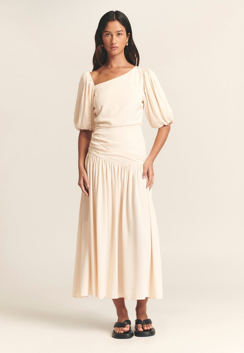 Krēmkrāsas midi kleita ar pūderveida piedurknēm un asimetrisku izgriezumu. Plūstoša silueta ar savilktu vidukli un mīkstu, gludu tekstūru.