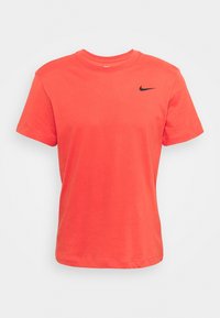 Jasnoróżowa koszulka Nike z krótkim rękawem i czarnym logo swoosh na lewej piersi, w stylu z okrągłym dekoltem, wyeksponowana na białym tle.