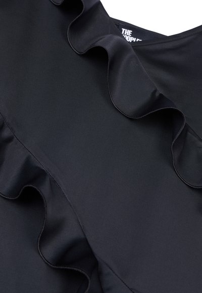 Top de tela negra con escote en V y un destacado borde de volantes a un lado, textura suave y una etiqueta que dice "THE PEOPLE."