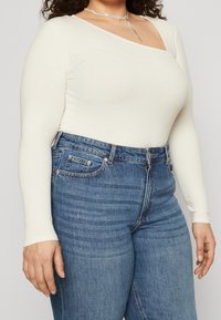 Crème-kleurige geribbelde lange mouwen bodysuit met een vierkante halslijn, gecombineerd met hoge taille blauwe jeans met een klassiek vijf-pocket ontwerp.