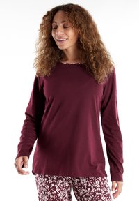 Maglietta a maniche lunghe color bordeaux realizzata in tessuto morbido con scollatura rotonda, abbinata a pantaloni bianchi con motivo floreale, caratterizzati da una vestibilità rilassata.