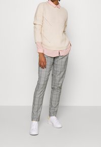 Krämfärgad stickad tröja, ljusrosa skjorta och grå rutiga byxor, kombinerat med vita sneakers med gula detaljer.