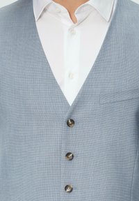 Helles blaues Weste aus strukturiertem Stoff. Verfügt über einen V-Ausschnitt, eine vierknöpfige Front mit dunklen Knöpfen und eine kleine Tasche auf der linken Seite.