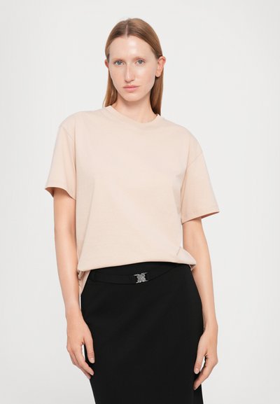 Short-sleeve, light pink cotton t-shirt with a classic crew neck, paired with a fitted black skirt featuring a decorative silver buckle.