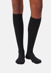 Schwarze knielange Socken mit geripptem Textur und glatter Oberfläche, ausgestattet mit einer verstärkten Spitze und einem Bündchen für Komfort und Langlebigkeit.