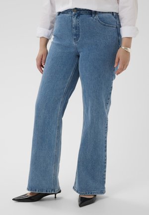 Højttaljede bukser med vide ben i lyseblåt denim. Har synlige sømme, fem lommer og en glat finish. Kombineret med sorte spidse hæle.