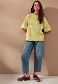 Oversize tričko so svetlo zelenými a béžovými pruhmi, voľné riflové nohavice a hnedé tenisky s čiernymi akcentmi. Jednoduchý dizajn, ležérny strih.