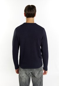 Marinblå stickad tröja med rund halsringning och långa ärmar, med en texturerad finish. Bärs med grå denimjeans.