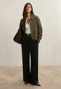 Oliviroheline seemisnahast jakk ees lukuga, mille all valge särk ja kõrge vöökohaga mustad laiade säärega püksid. Pruun käekott ja teravnurkade kontsakingad.