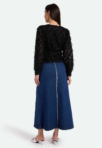 Top negro texturizado de manga larga con una cintura ajustada, combinado con una falda larga de denim azul que presenta una costura central en contraste y un dobladillo deshilachado.