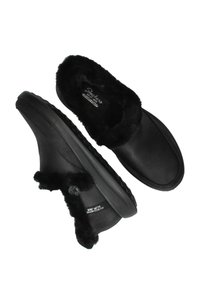 Zapatillas negras de casa tipo slip-on, con un suave puño y forro de piel sintética, textura lisa y suela de goma texturizada con detalle de logo.