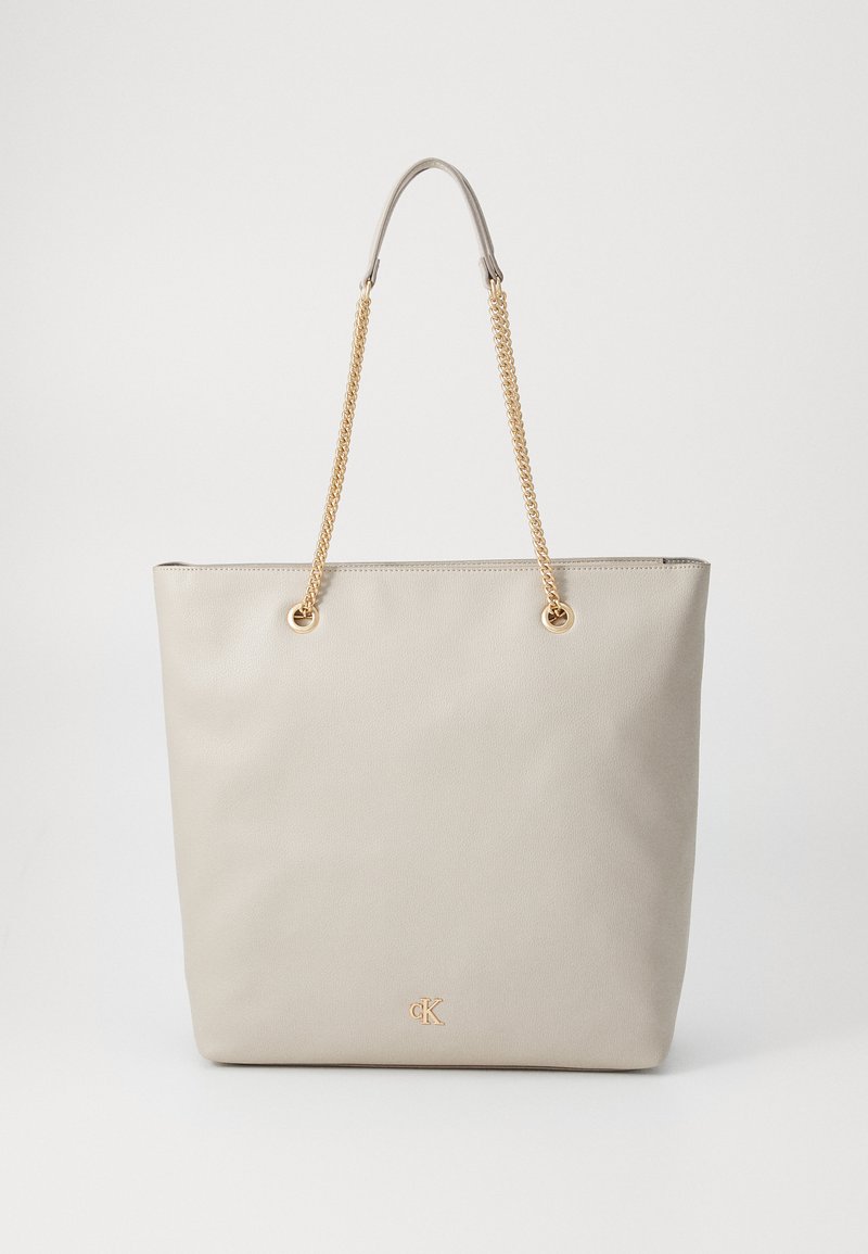 Beige tote bag with textured faux leather, minimalist design, gold chain straps, and subtle logo in the lower corner. Flat and structured shape.