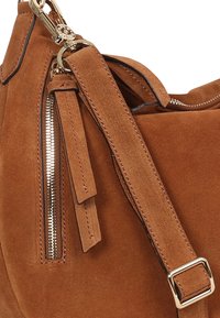 Braune Veloursleder-Handtasche mit glatter Textur, betonter Reißverschluss und verstellbarem Riemen mit Metallschnalle. Seitlicher Fransenbesatz sorgt für ein interessantes Detail.