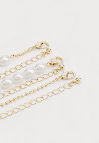 Cadenas de metal dorado y cuentas de perla con cierres de langosta, mostrando una mezcla de eslabones redondos y alargados en texturas y tamaños variados.