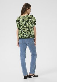 Grøn camouflage-mønstret kortærmet skjorte parret med lysblå straight-leg jeans og sorte blokhælede sko. Glat stoftekstur.