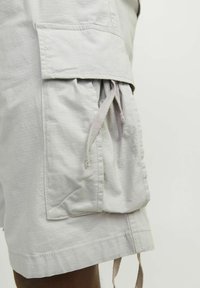 Lys grå cargo shorts lavet af tekstureret stof med snørredetalje på sidelommerne og syet kant.