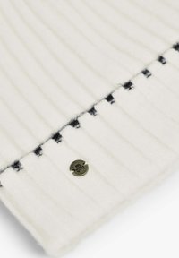 Tejido de punto ribeteado blanco con una textura suave, con costuras de acento negras y un botón metálico redondo con un diseño de calavera.