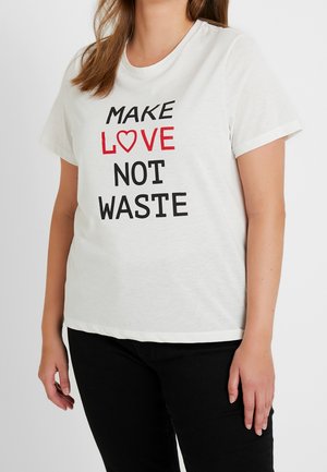 Kobieta w białej koszulce z czarnym i czerwonym napisem „MAKE LOVE NOT WASTE”, czerwonym symbolem serca zamiast litery O w słowie LOVE, w połączeniu z czarnymi spodniami.