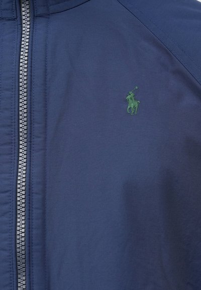 Navy blue zip-up jacket made of smooth fabric, featuring a green embroidered logo and contrasting zipper.
