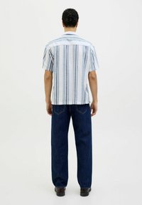 Camicia a maniche corte con righe verticali blu e bianche, tessuto leggero, vestibilità comoda, abbinata a jeans dritti blu scuro.