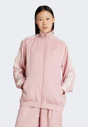Pink zip-up jacket made of smooth material, featuring three white stripes along the sleeves and an embroidered logo on the chest.