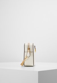Piccola borsa a tracolla in pelle bianca con dettagli in oro, mostrata di lato su un piedistallo bianco contro uno sfondo semplice.