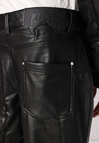 Schwarze Lederhosen mit glatter Textur, hohem Bund und dekorativer Naht, sowie einer Gesäßtasche mit silbernem Akzent.