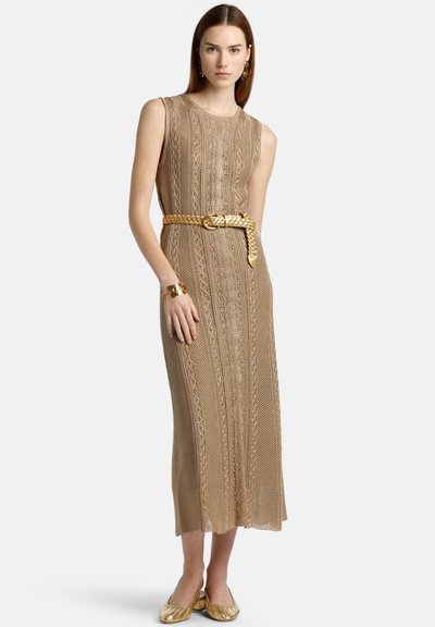 Robe sans manches en tricot beige avec des motifs complexes et une ceinture dorée tressée. Accentuée par une finition texturée, portée avec des ballerines dorées assorties.