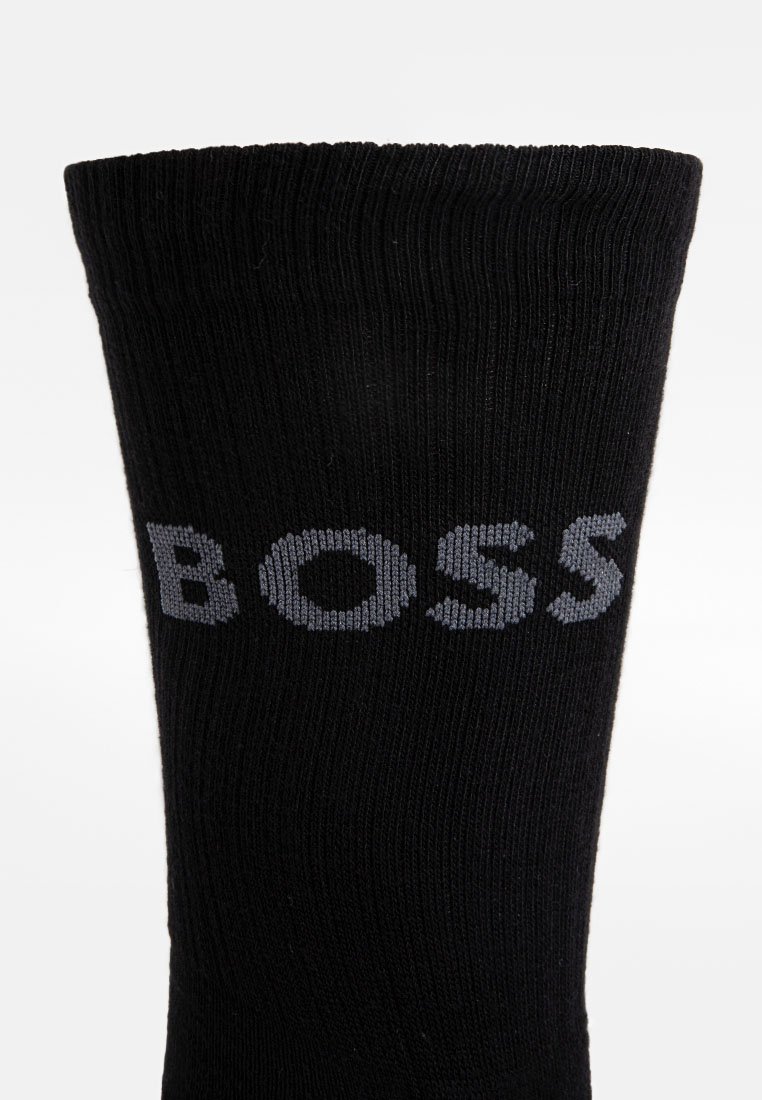 Schwarze gerippte Socke mit grauem gestricktem "BOSS"-Logo nahe der oberen Kante auf einem schlichten weißen Hintergrund.
