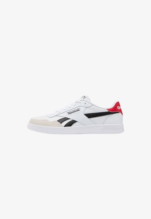 Witte Reebok sneaker met zwarte strepen, beige teenaccent, rode hieltab en witte zool getoond in zijaanzicht.